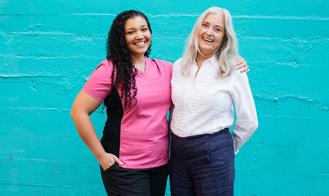 Caregiver next to an elderly woman while being outside behind a turquoise wall